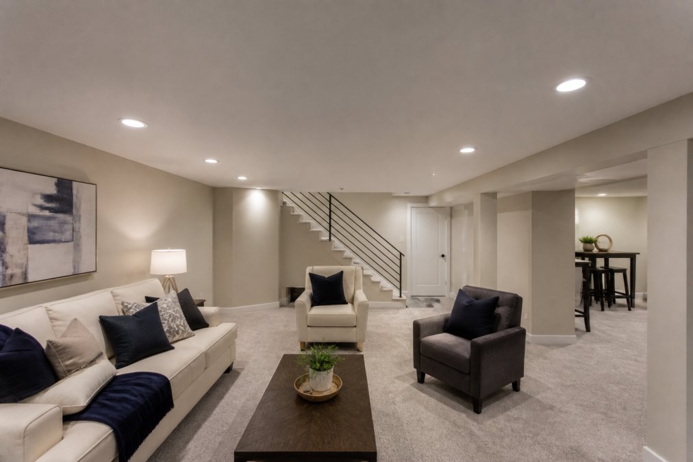 A finished basement with a low ceiling featuring ultra-thin recessed wafer LED downlights, showing a clean flush ceiling surface and a cozy seating area below