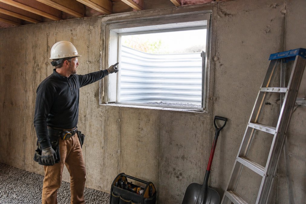 Contractor inspecting an egress window well in a basement rental unit to ensure fire safety code compliance