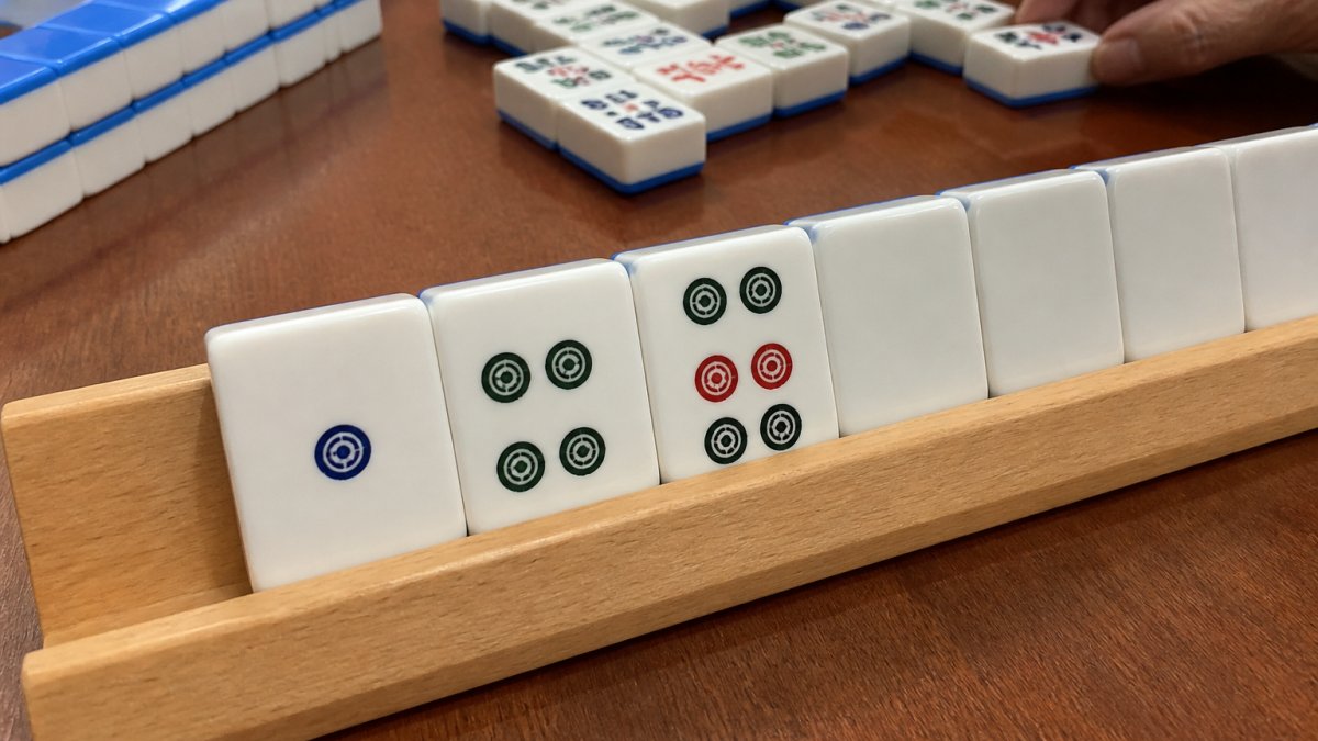 Close-up of Mahjong tiles arranged on a wooden table showing the 1-4-7 numerical pattern clearly visible in one suit, with a player's hand rack and discard pile visible in soft natural lighting