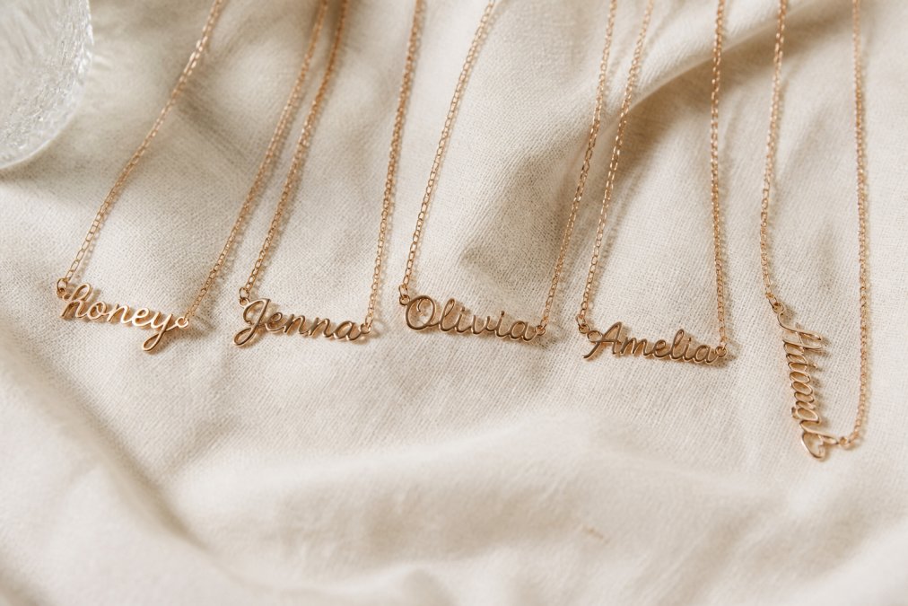 Five personalized rose gold name necklaces arranged on a cream linen surface