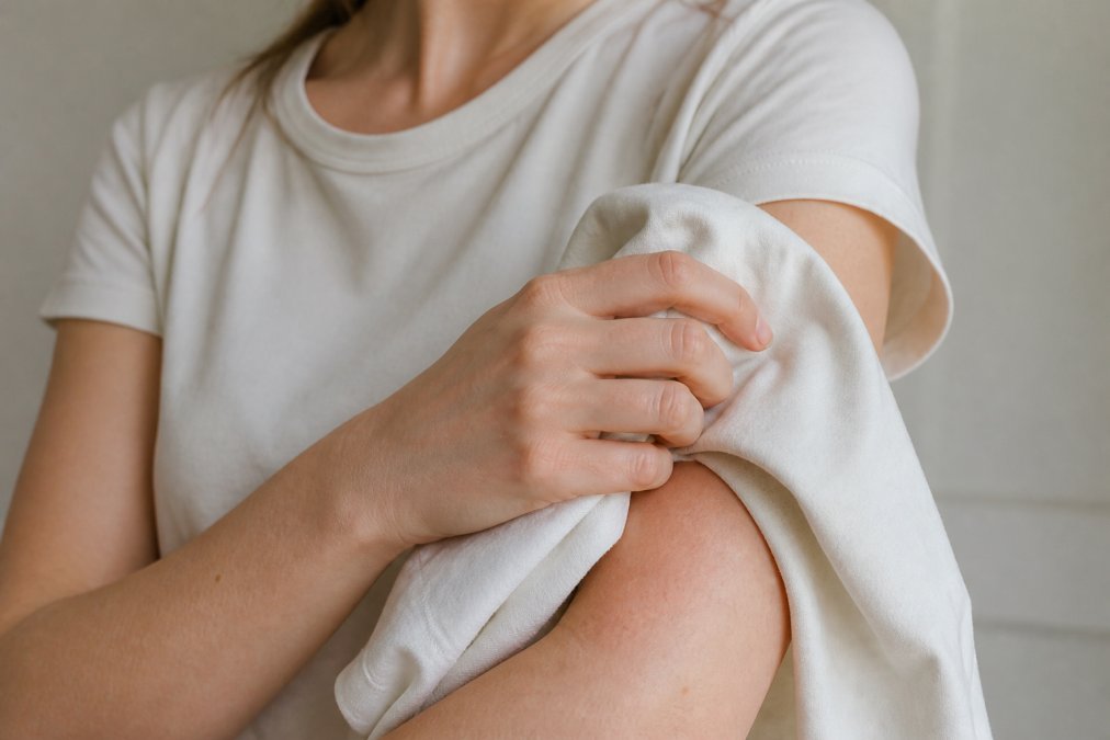 Close-up of a person with sensitive skin gently holding a soft organic cotton t-shirt against their forearm in natural light, showing the smooth fabric texture