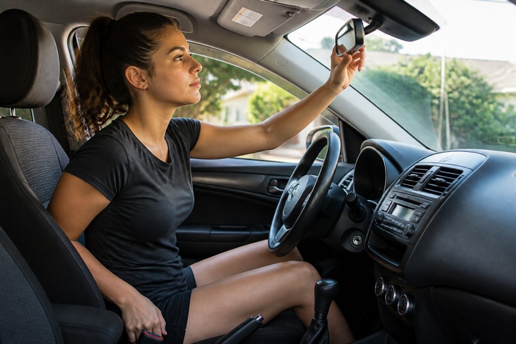 New driver adjusting seat position and mirrors for driving practice drills inside a car cabin