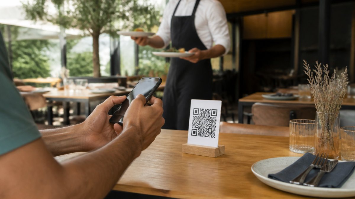 Cliente escaneando un código QR en la mesa de un restaurante moderno mientras el camarero sirve los platos