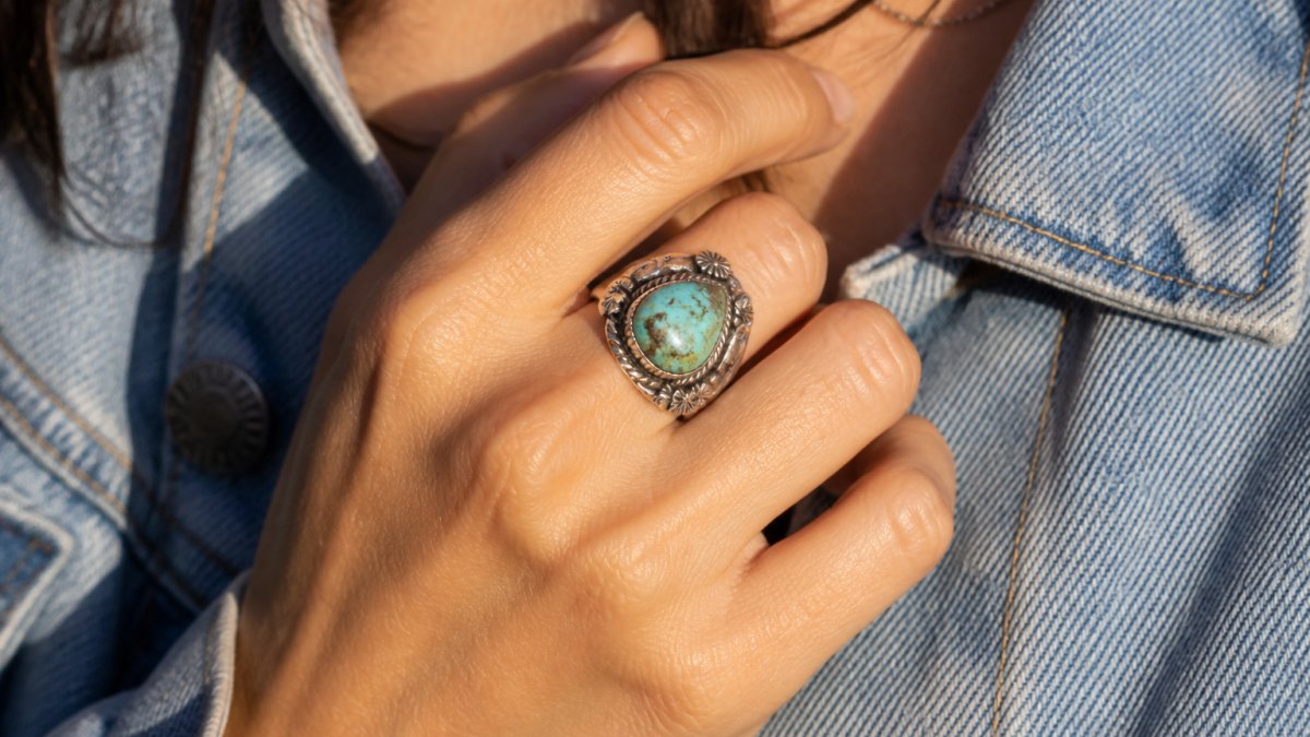Close-up of a woman's hand wearing a handcrafted sterling silver turquoise ring with natural stone detail and intricate silverwork, photographed in warm natural sunlight