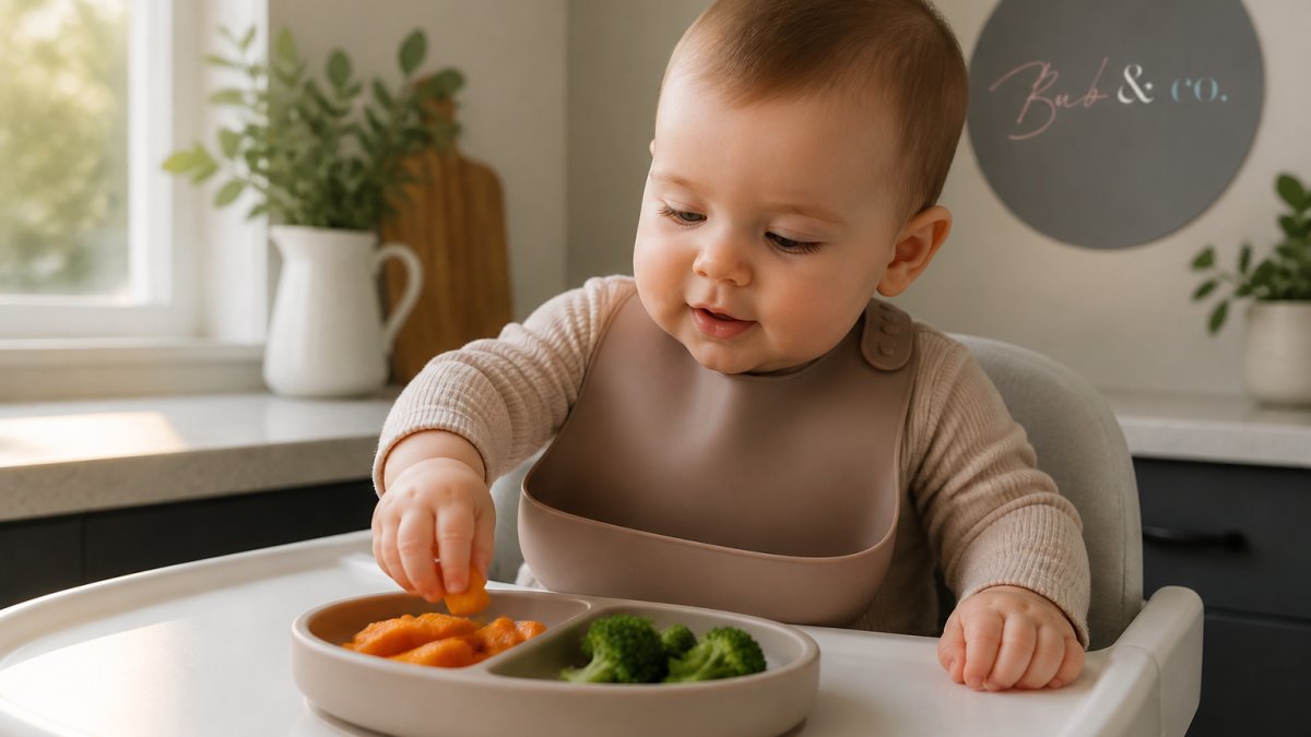 An 8-month-old baby sitting in a highchair, reaching for soft pieces of sweet potato and broccoli on a suction plate, wearing a silicone bib, soft morning light through a kitchen window