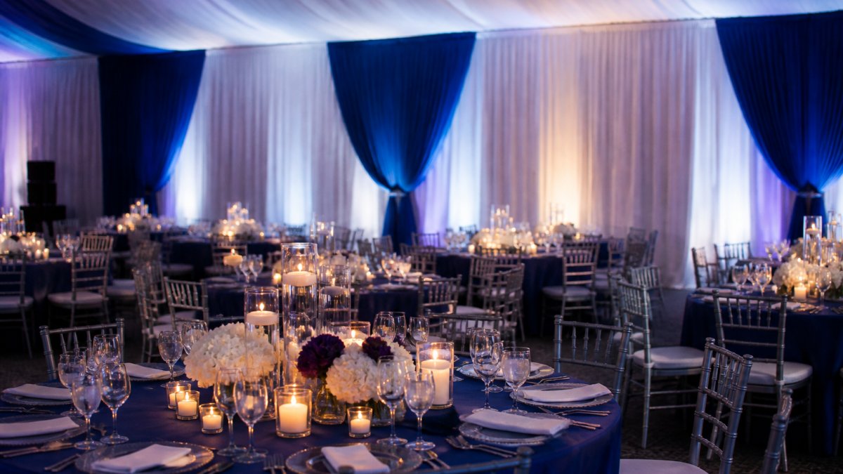 Elegant gala venue featuring layered blue and white corporate event draping with candlelit tables and ambient lighting.