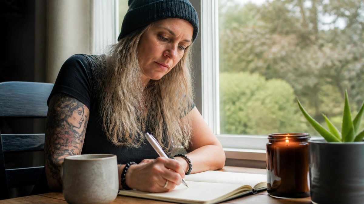 Woman in her forties resting peacefully with a cup of tea, modelling a cosy beanie in a quiet, grounded space.