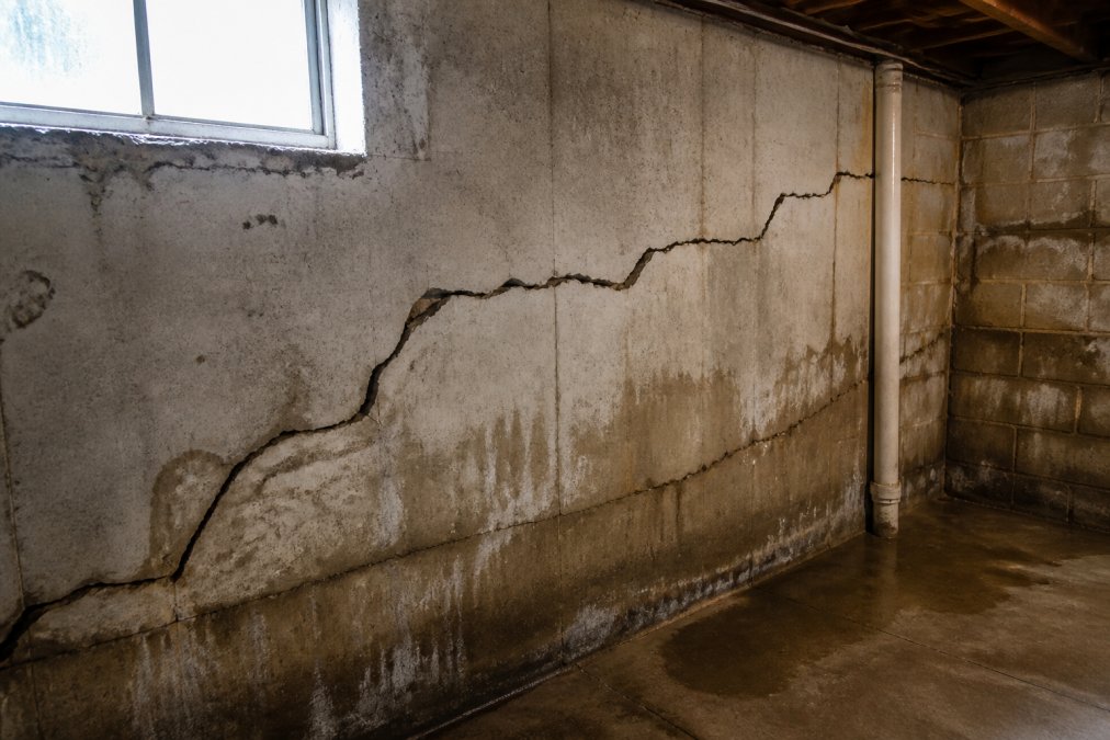 Close-up of cracked foundation wall with visible structural damage and water staining on interior basement wall under natural light