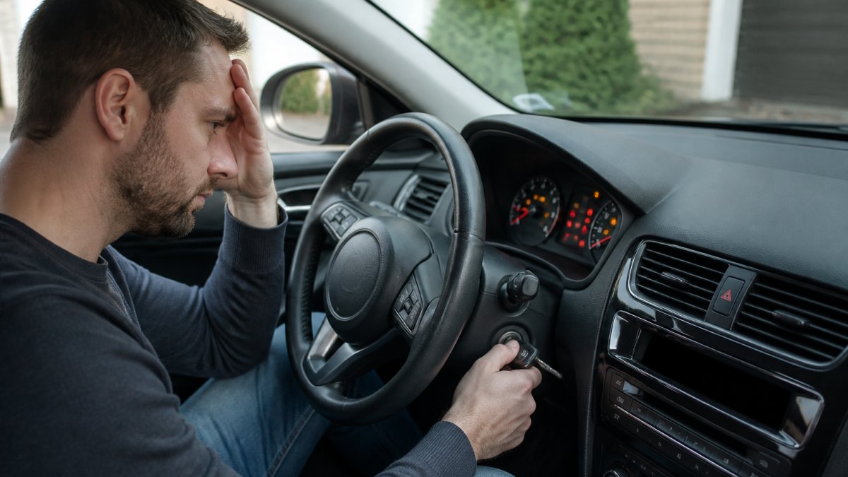 A driver sitting in the front seat of a modern car, hand on the ignition, dashboard warning lights glowing, looking concerned as the engine fails to start