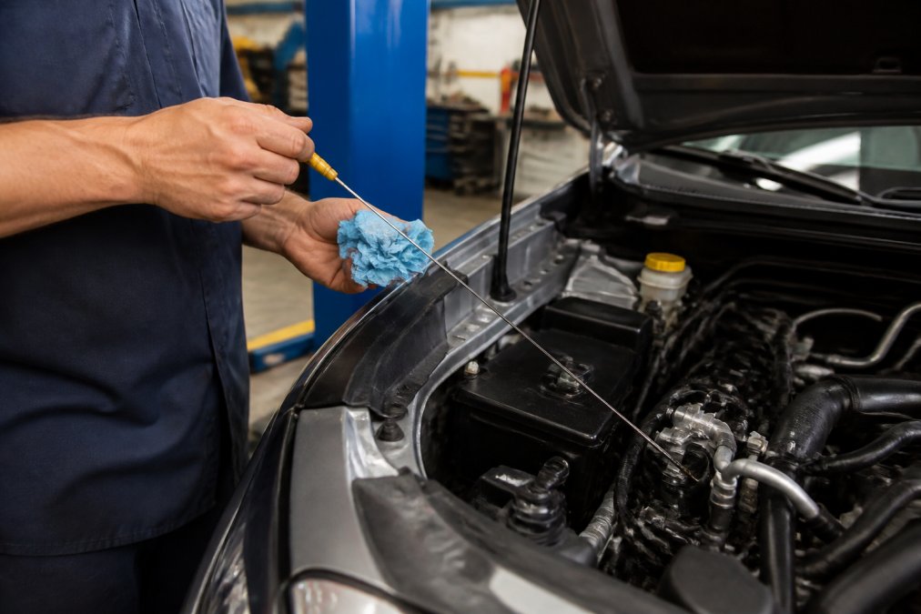 Professional technician's hands checking transmission fluid level with a yellow dipstick under the open hood of a Subaru, natural shop lighting illuminating the engine bay