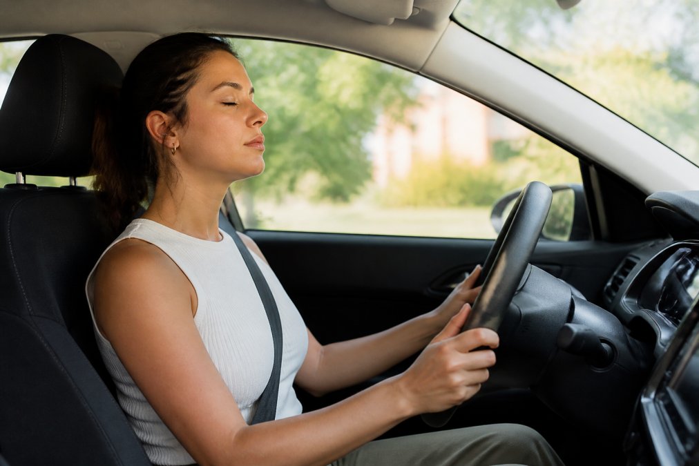 A calm driver sitting in the driver's seat with eyes closed, taking a deep breath before starting the car, hands relaxed on the steering wheel, soft daylight through the windshield