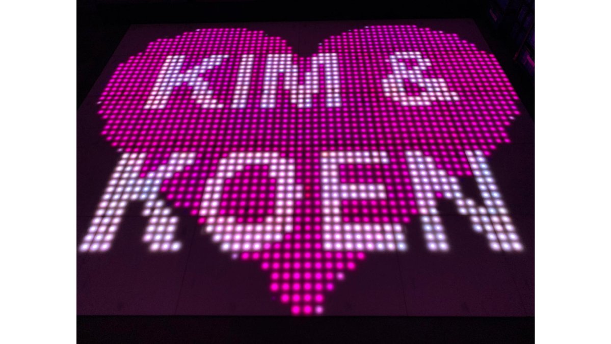 Bruidspaar dansend op een verlichte 100 Pixel Discovloer met fel gekleurde LED-effecten, omringd door gasten die toekijken en foto's maken, warm sfeervolle verlichting in feestzaal