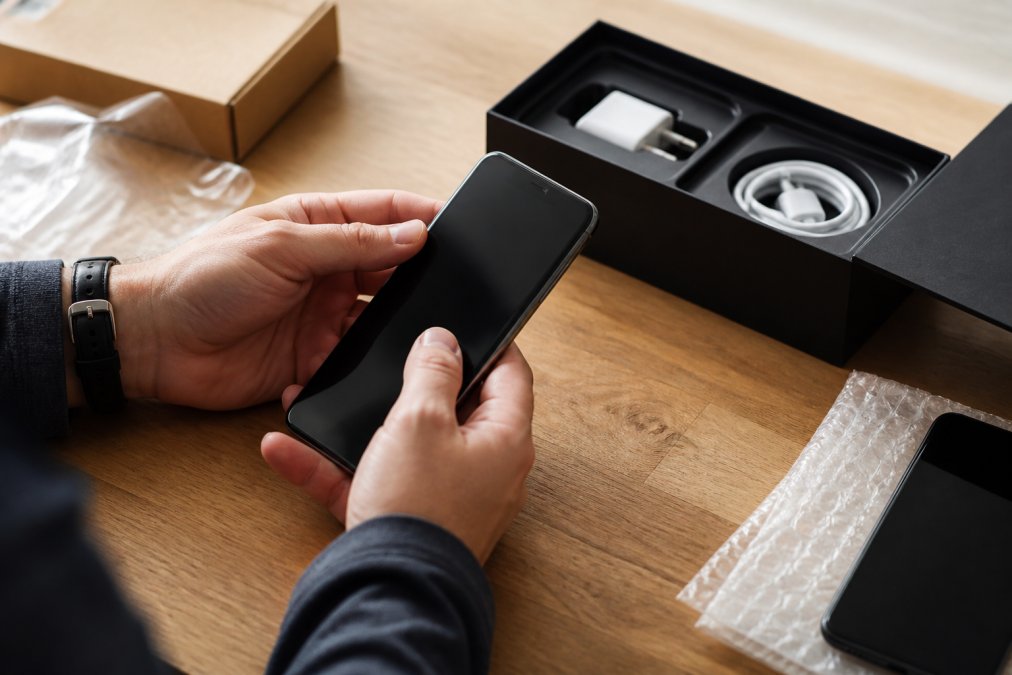 Close-up of hands inspecting a refurbished smartphone, checking the screen responsiveness and examining the device condition on a clean work surface with natural lighting
