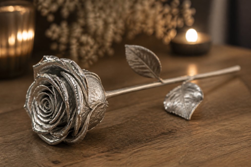 A silver-dipped preserved rose displayed on a wooden surface with soft ambient lighting, showing the intricate detail of the silver coating on the delicate rose petals
