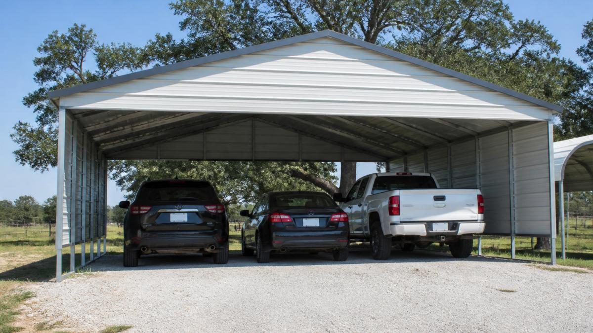 Wide-angle view of a completed metal 30x20 carport with galvanized steel frame sheltering three parked vehicles, showing open-front design and gable roof against clear sky