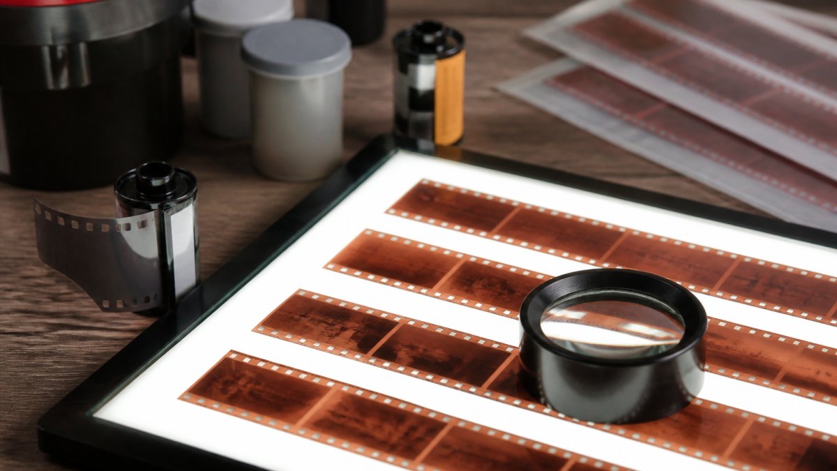 Een filmrol en negatievenstroken op een lichtbak met een loep voor kwaliteitscontrole van analoge opnames