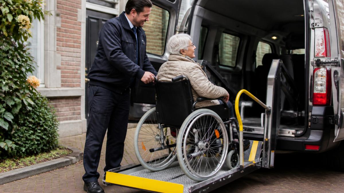 Chauffeur helpt oudere dame bij veilig rolstoelvervoer in een aangepaste taxi met lift in Utrecht.