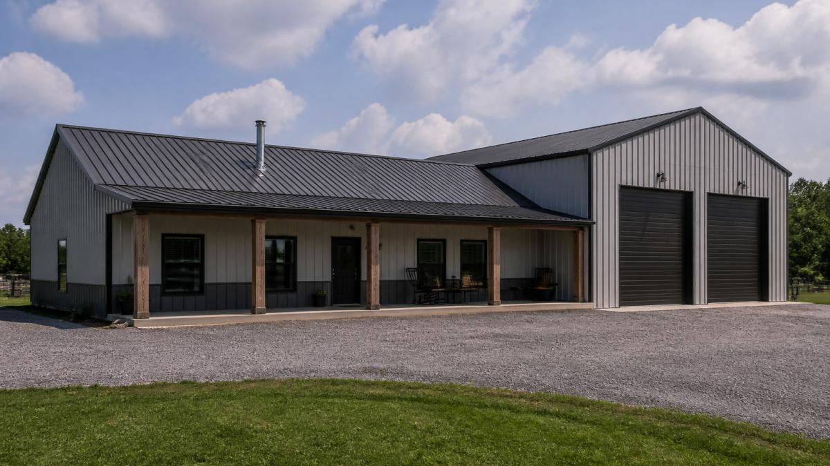Completed metal barndominium with steel siding and metal roof showing residential section with windows and workshop bay doors, photographed from exterior in natural daylight