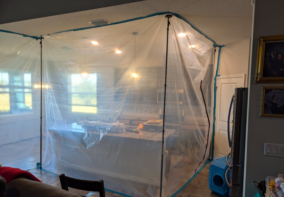 Mold remediation containment setup inside a residential home. Clear plastic containment barriers isolate the work area, with professional air filtration equipment visible. Actual JLX Environmental remediation project in Sebastian, Florida.
