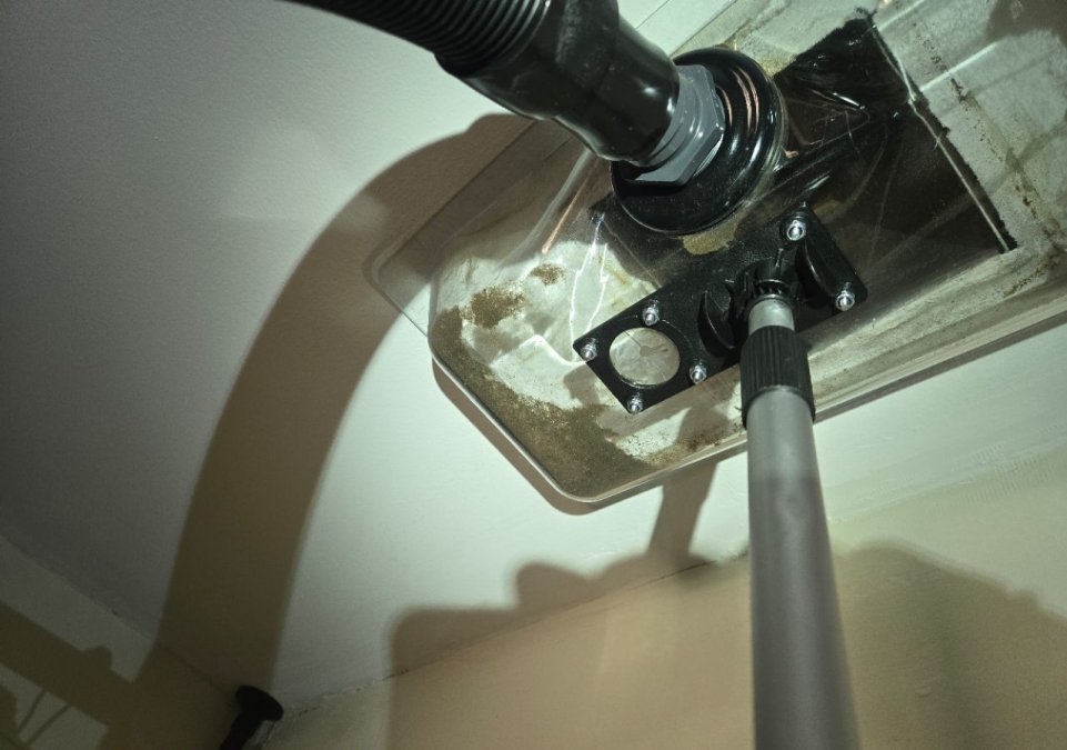 Professional air duct cleaning using a clear collection hood and vacuum system at a residential HVAC vent.