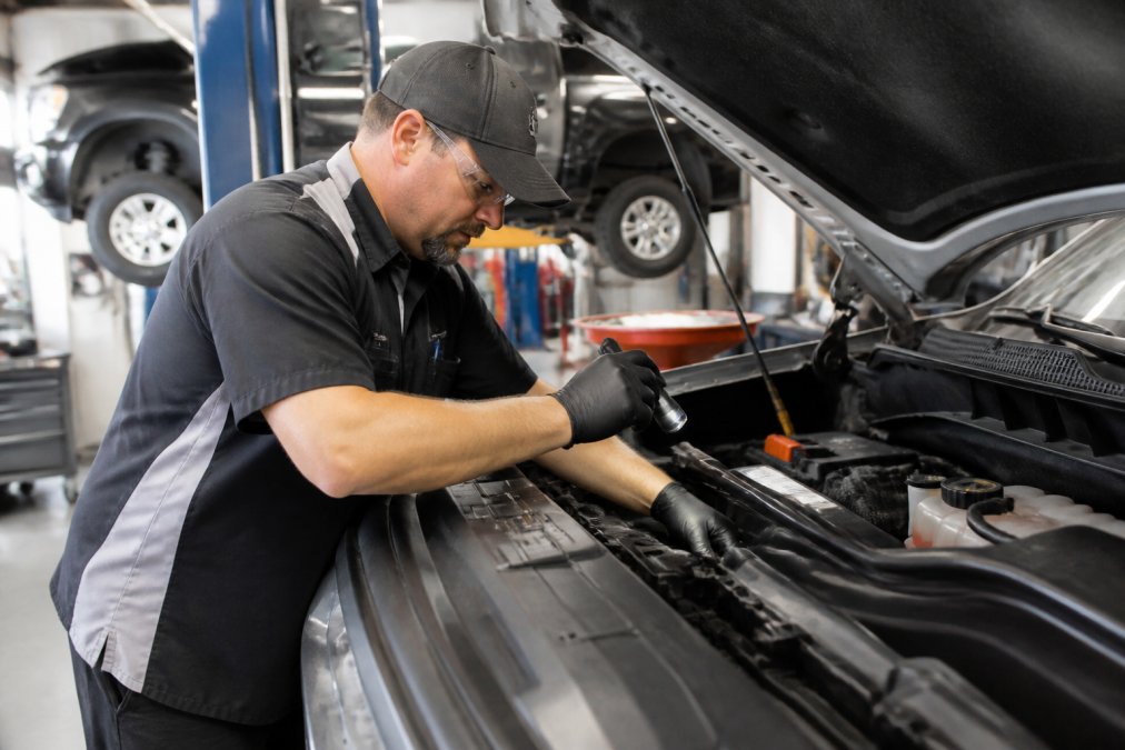 Professional certified technician in uniform performing routine vehicle inspection and maintenance service in a modern professional service bay with proper lighting