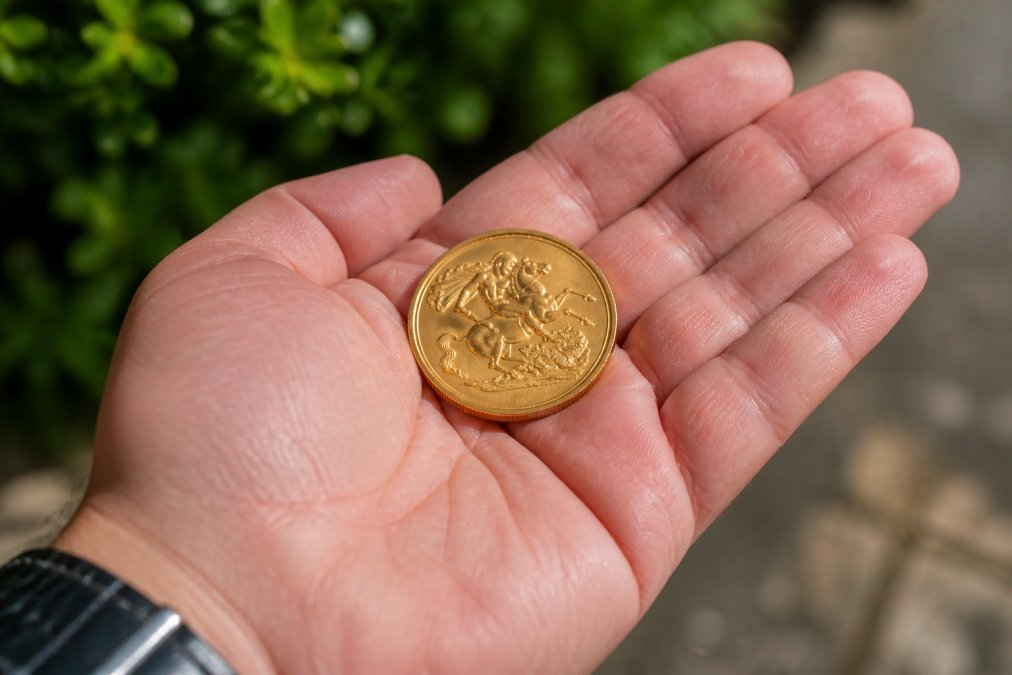 Close-up of a polished gold sovereign coin resting in an open palm, with soft natural light highlighting the coin's intricate detail and lustrous surface