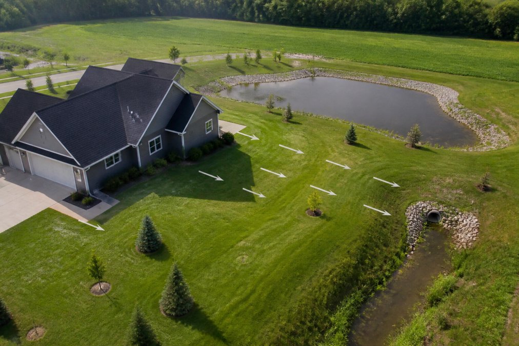 Aerial view of residential property showing proper grading slopes with water runoff flowing away from the foundation toward a drainage system and retention area