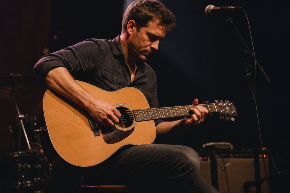 Professional musician playing a steel-string guitar on a stage, representing top acoustic guitar brands.
