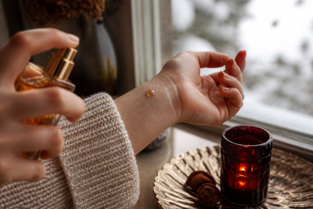 A drop of golden perfume on a wrist against a cozy wool sweater in soft winter light