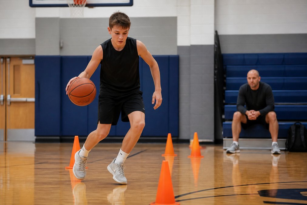 Young basketball player practicing dribbling drills between cones as part of basketball training exercises.