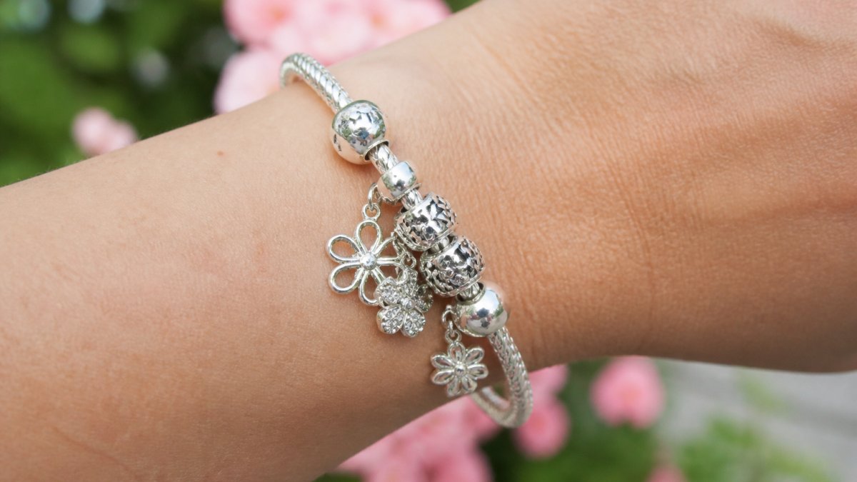 Close-up of a polished sterling silver charm bracelet on a wrist, showing individual dangle charms and the metallic finish in natural light