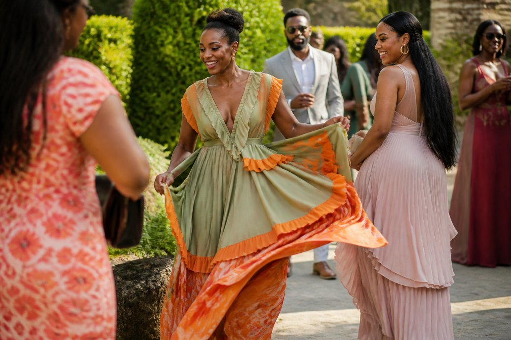 Woman in flowing sage green and orange cotton maxi dress with delicate ruffle detailing, fabric captured mid-movement in natural sunlight to show texture and the interplay between the two colors