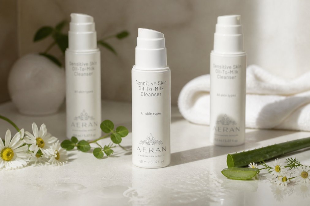 Three cleanser bottles arranged on light surface with water droplets and fresh botanical ingredients nearby, showing product textures and packaging