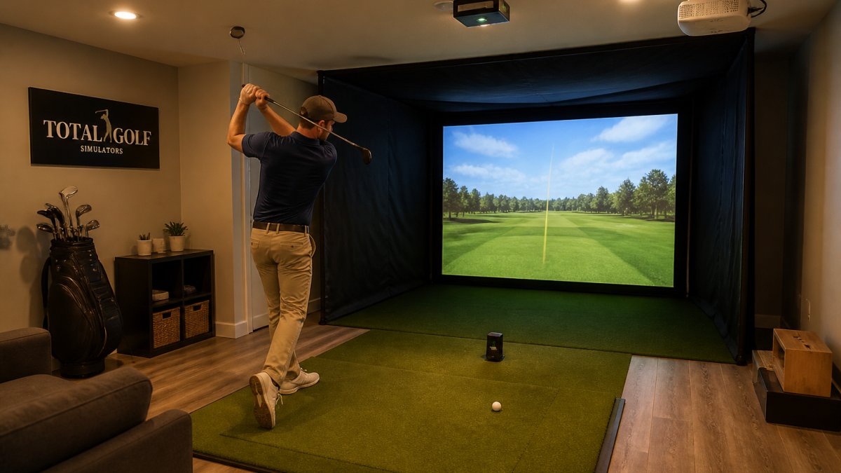 Golfer mid-swing inside a compact basement simulator enclosure with overhead launch monitor and projector