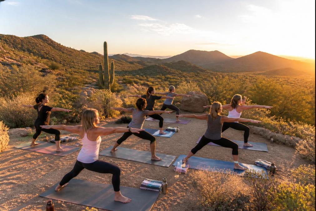 Women practicing yoga outdoors in a desert setting at sunrise, with mountains in the background, demonstrating mindfulness and peaceful movement in synchronized poses