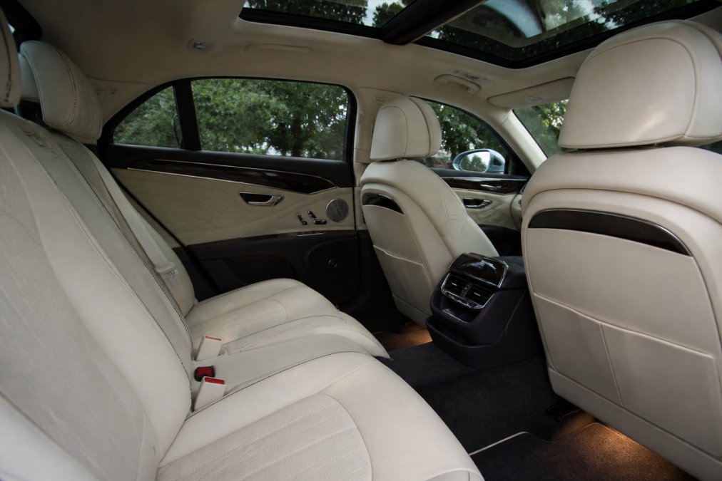 Interior of a prestige luxury vehicle showing cream leather seats with contrast stitching, ambient footwell lighting, a polished centre console, and a panoramic sunroof, conveying bespoke comfort and quiet prestige