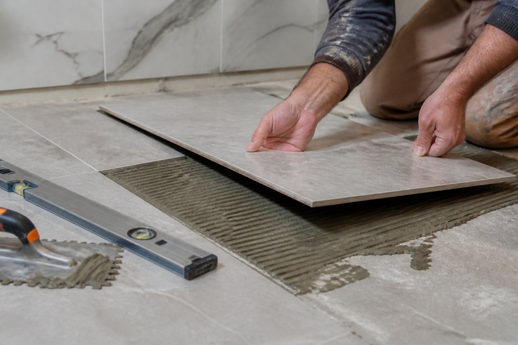 Renovator applying adhesive to install moisture resistant porcelain tile on a bathroom floor