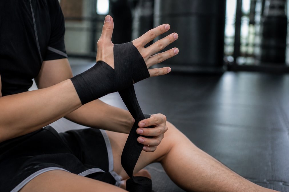 Close-up of a beginner MMA fighter's hands showing proper hand wrapping technique before putting on BRAVE MMA Competition Gloves, with focus on wrist stabilization and padding alignment during training session