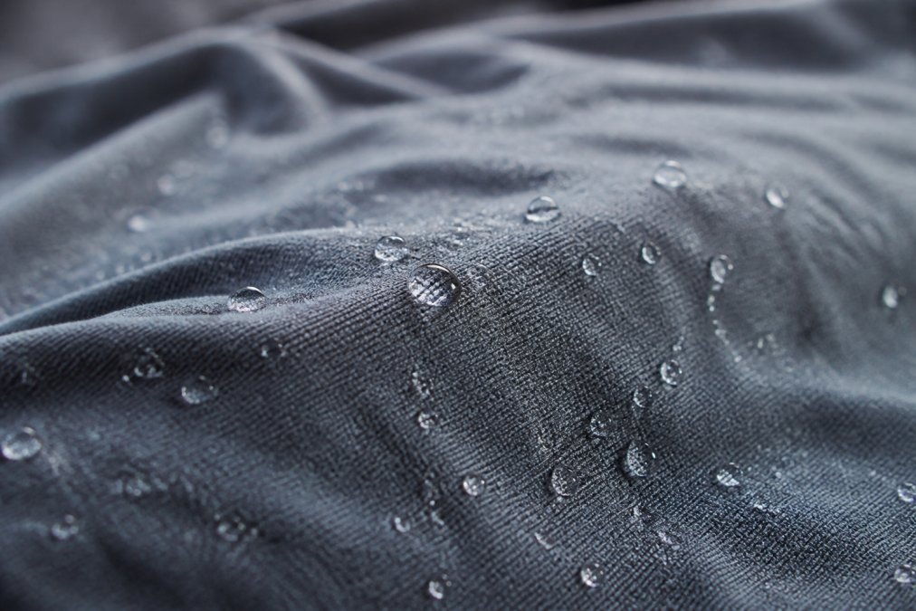 Close-up of a moisture-wicking fabric being tested, showing sweat beading on the surface and quick-drying properties with visible hydrophobic water droplets on the synthetic material