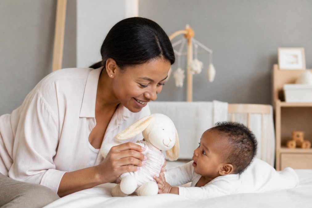 A parent holding a soft, organic cotton plush toy next to a newborn baby in a bright, clean nursery setting