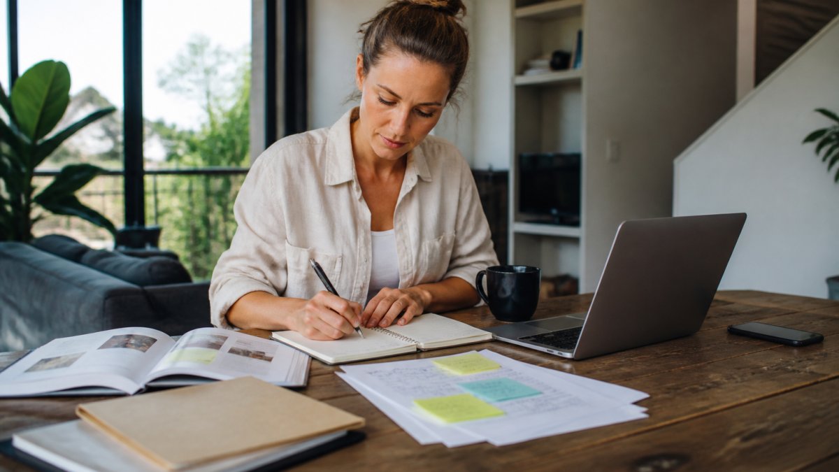 Service business founder working at desk with laptop, planning documents, and strategy notes visible, showing focused work on business systems and operational planning