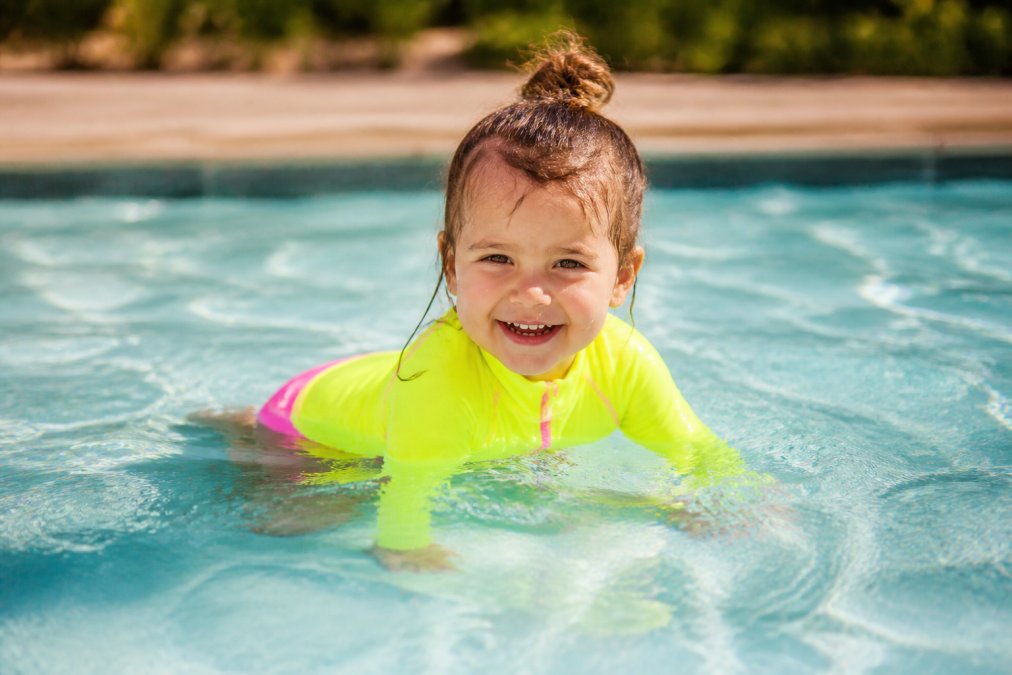 Toddler wearing bright high-visibility swimsuit and rash guard in the water, showing vibrant colors and UPF protection in clear daylight