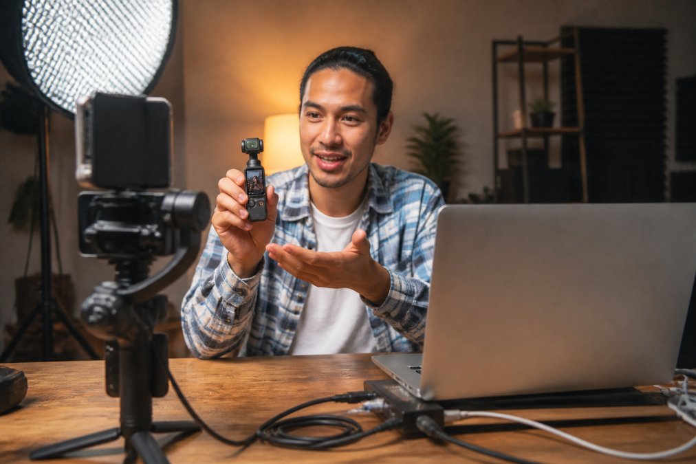 Professional content creator filming with a streaming camera setup on a desk with professional LED lighting, HDMI cables connected to a laptop displaying streaming software, organized cable management visible