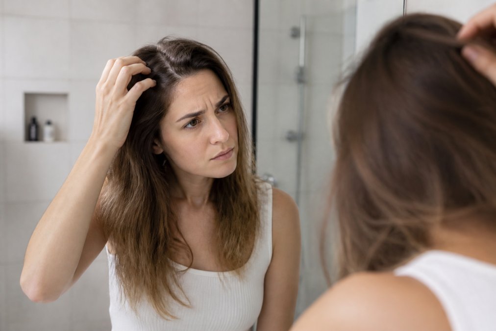 Woman looking in a mirror while gently touching her irritated sensitive scalp