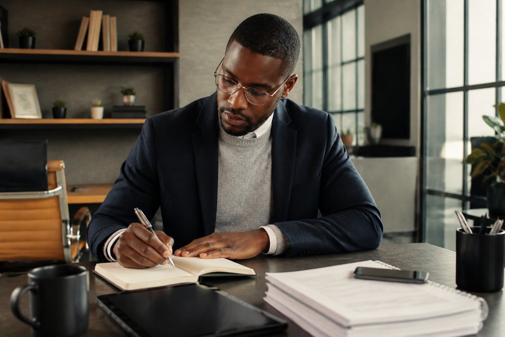 Man wearing a faith-based sweater layered with a blazer in a modern office environment, sitting at a desk with professional lighting, demonstrating how to adapt spiritual apparel for work