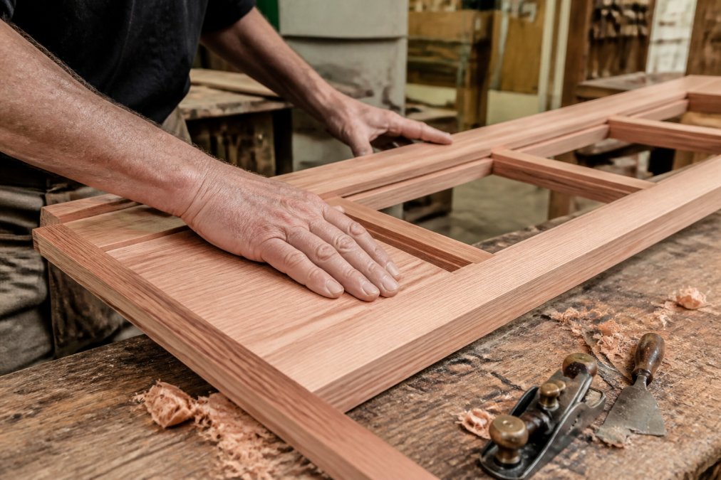 Joiner’s hands feeling the grain of European Redwood for a period window restoration project in a workshop.