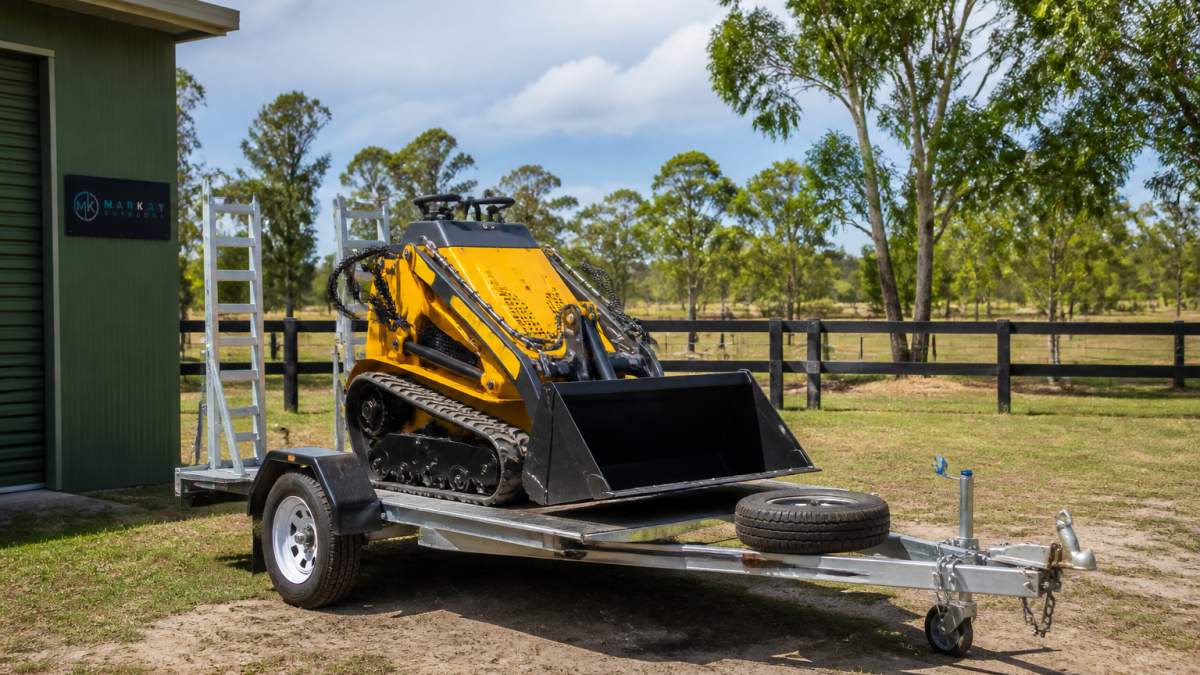 Compact Kanga mini loader on a single-axle trailer parked on a rural property with open yard space and fencing visible, ready for collection