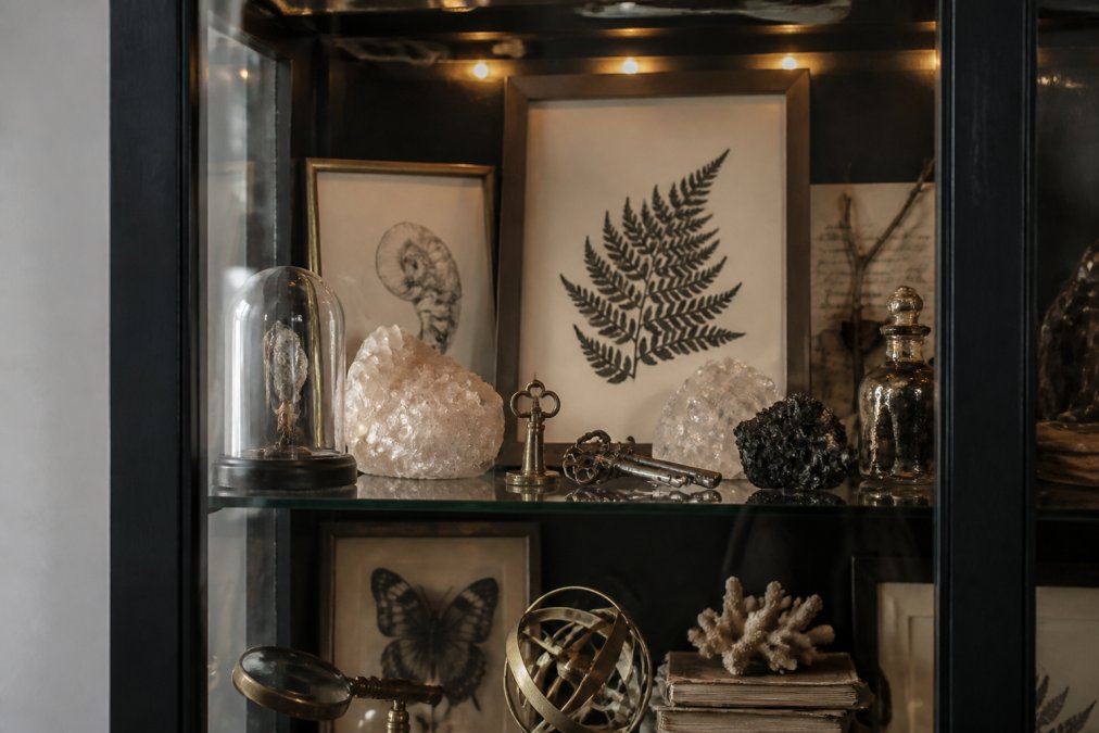 Close-up of a curated curiosity cabinet display featuring minerals, vintage keys, and framed prints under soft LEDs.
