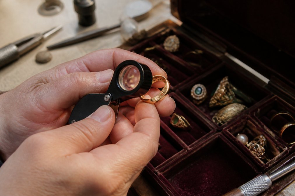 Close-up of a jeweler's loupe held over a vintage gold ring, revealing tiny hallmark stamps on the inner band, with soft natural light and a velvet tray in the background