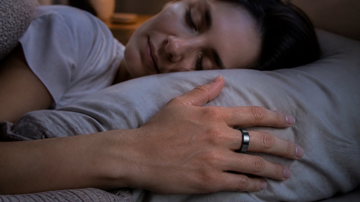 Close-up of a person's hand wearing a sleek titanium ring while resting on a soft pillow, calm dim bedroom background